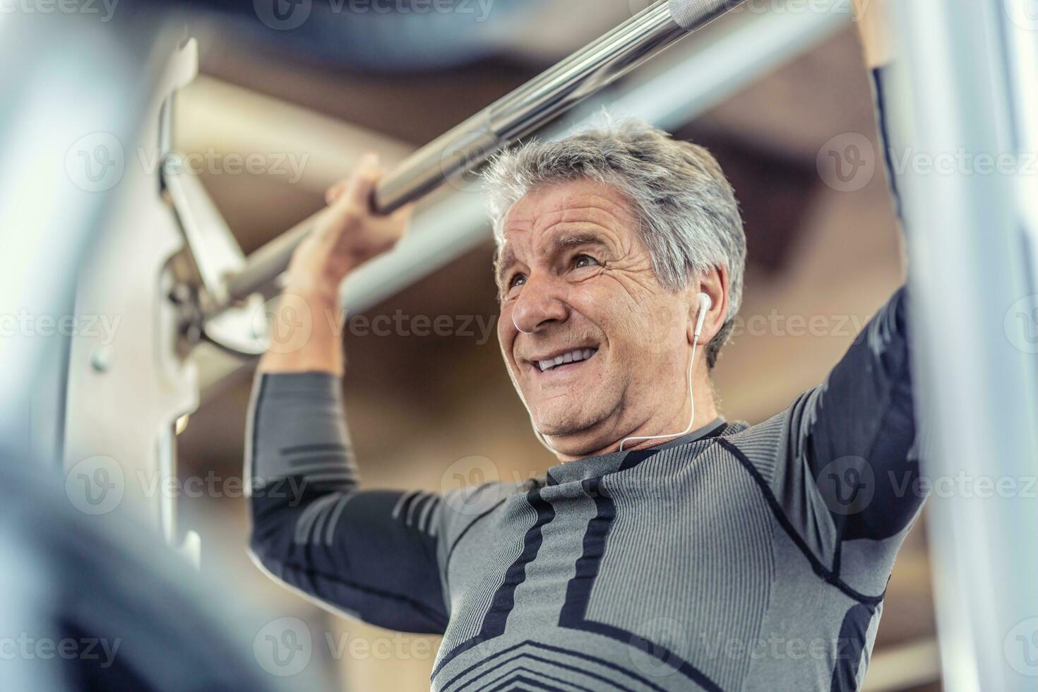 Exercising shoulders strength by an older man on a fitness machine inside the gym photo