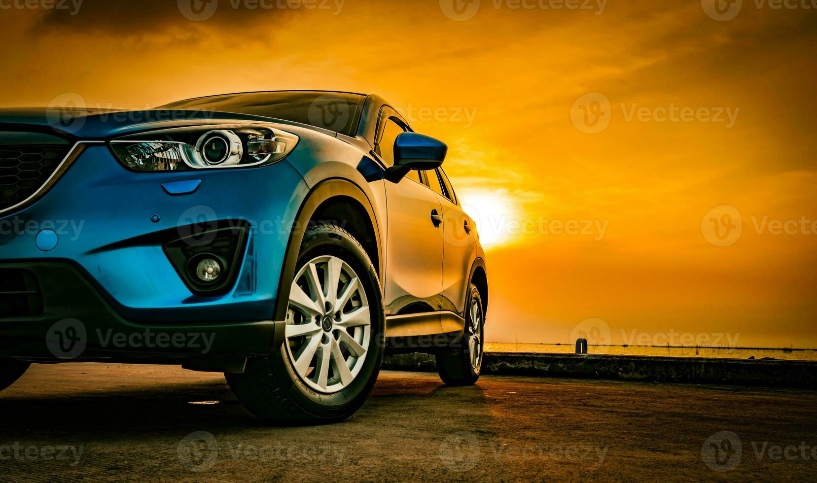 Blue compact SUV car with sport and modern design parked on concrete road by the sea at sunset. Environmentally friendly technology. Business success concept. photo