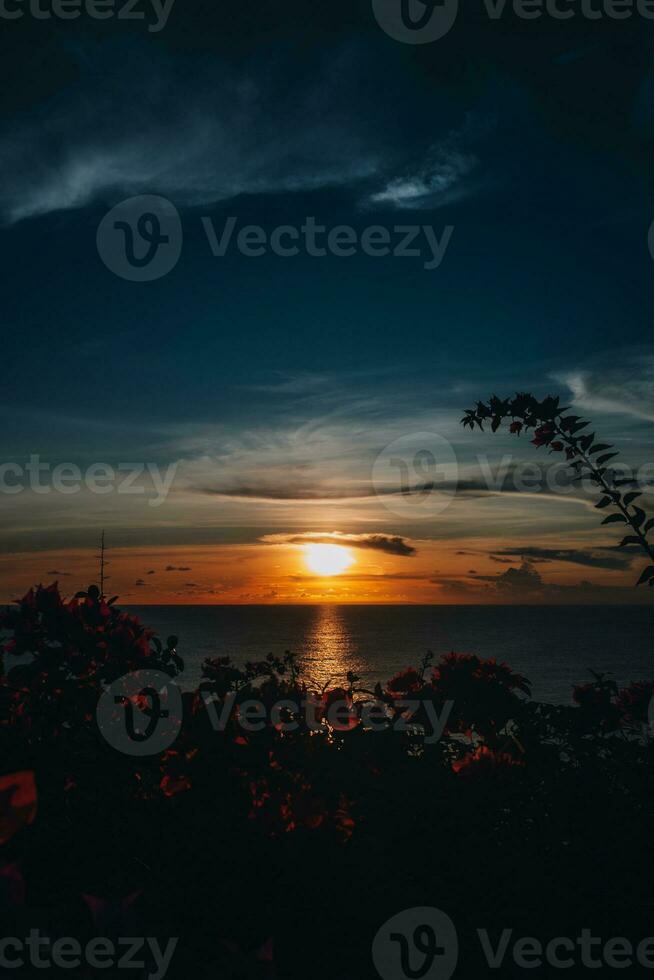 Bright orange sunset on the dark Indian Ocean on Bali island. Evening sunlight, fire sky, amazing view with flowers photo