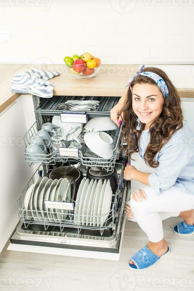 joven mujer utilizando un lavavajillas en su moderno cocina foto