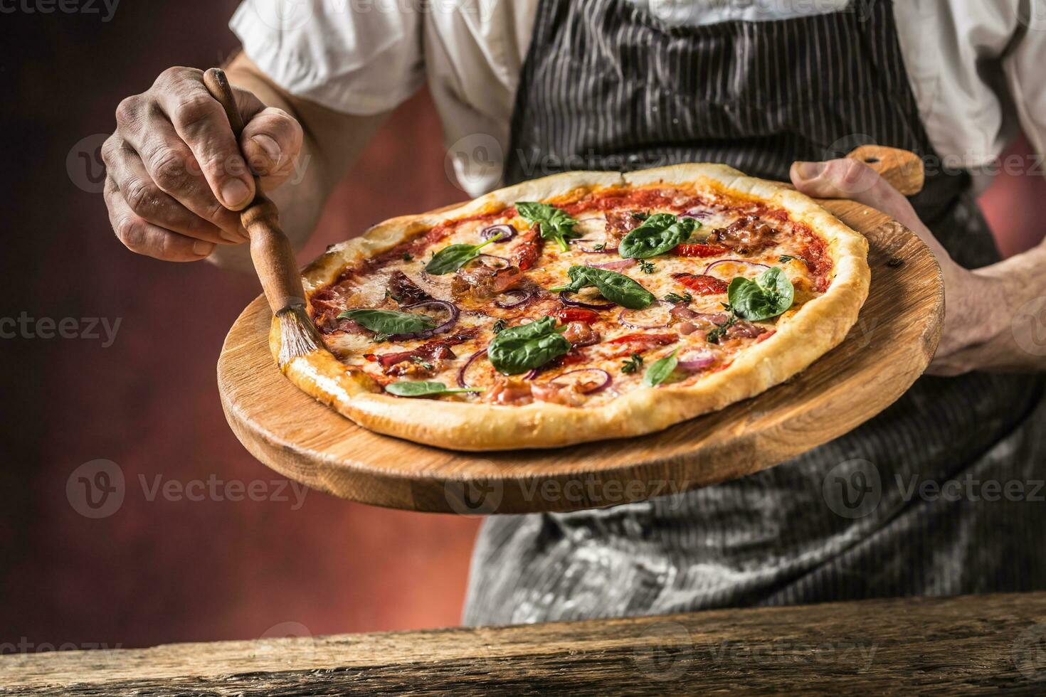 Pizza y cocinero. cocinero en el restaurante prepara un Pizza y decora eso con aceituna petróleo foto