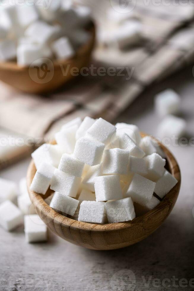 blanco azúcar cubitos en un de madera cuenco en el mesa foto