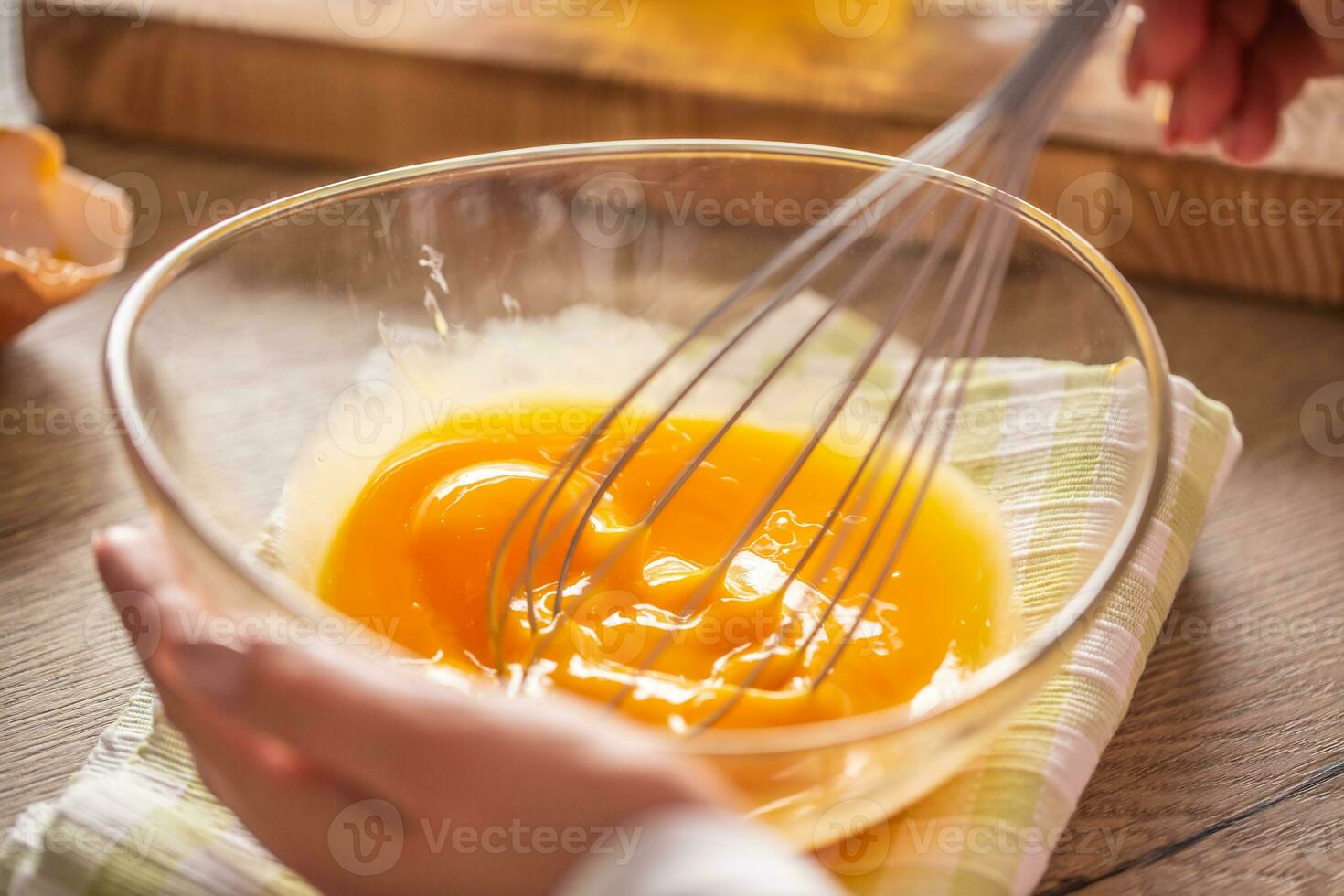 Detail of eggs being whisked in a bowl placed on a towel and wooden table photo