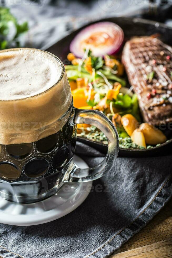 Glass of dark beer in pub or restavurant on table with delicoius food photo