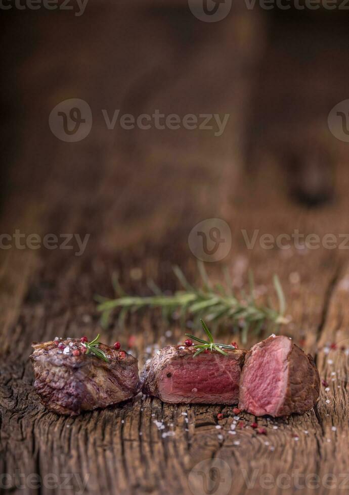 Grilled beef steak with rosemary, salt and pepper on old cutting board. Beef tenderloin steak. photo