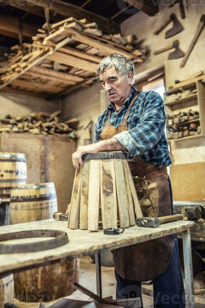 Old craftsman builds a new wooden barrel from metal and lumber in an old-fashioned way photo