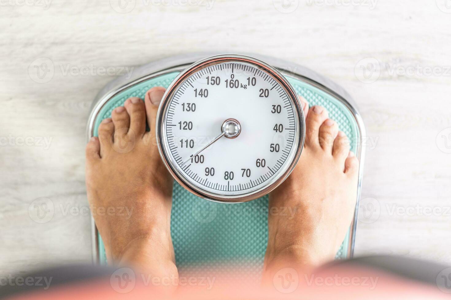 Woman looks down at the number of pounds or kilograms as she stands on a weighing scale photo