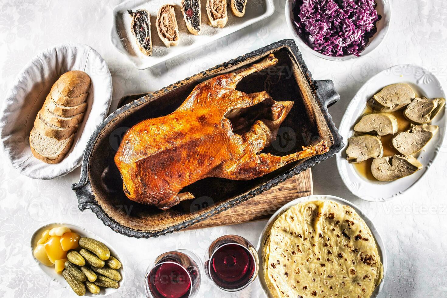 Roast goose with side dishes, red cabbage, roast, strudel, potato dumplings, pickles, bread and red wine. Traditional holiday food. Top view photo