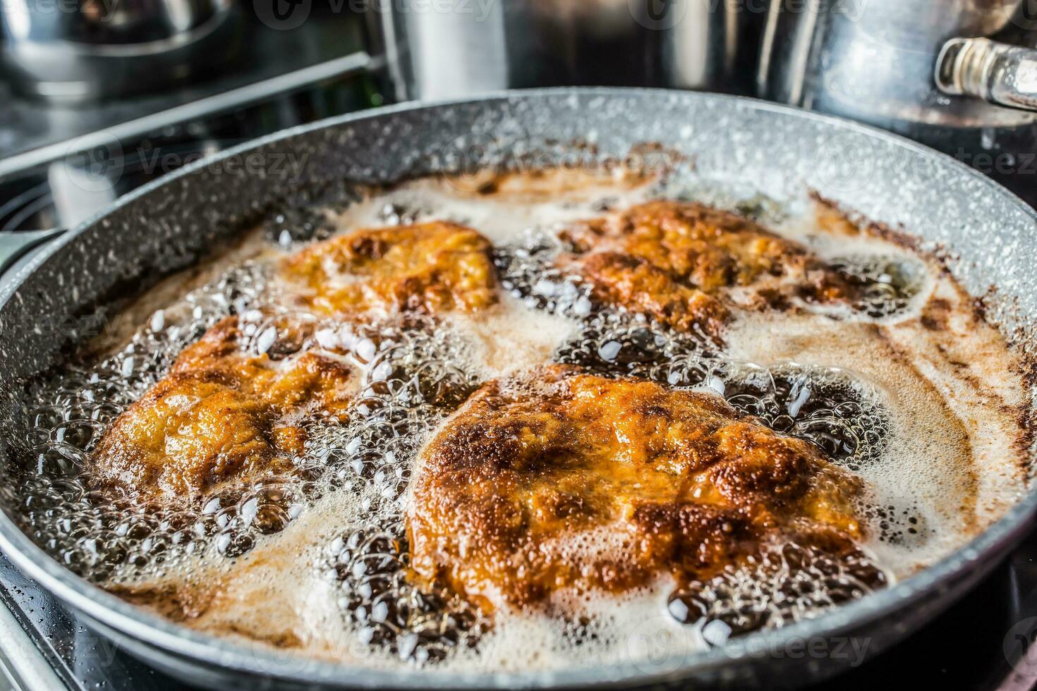 Schnitzels being fried in oil inside a dark pan photo