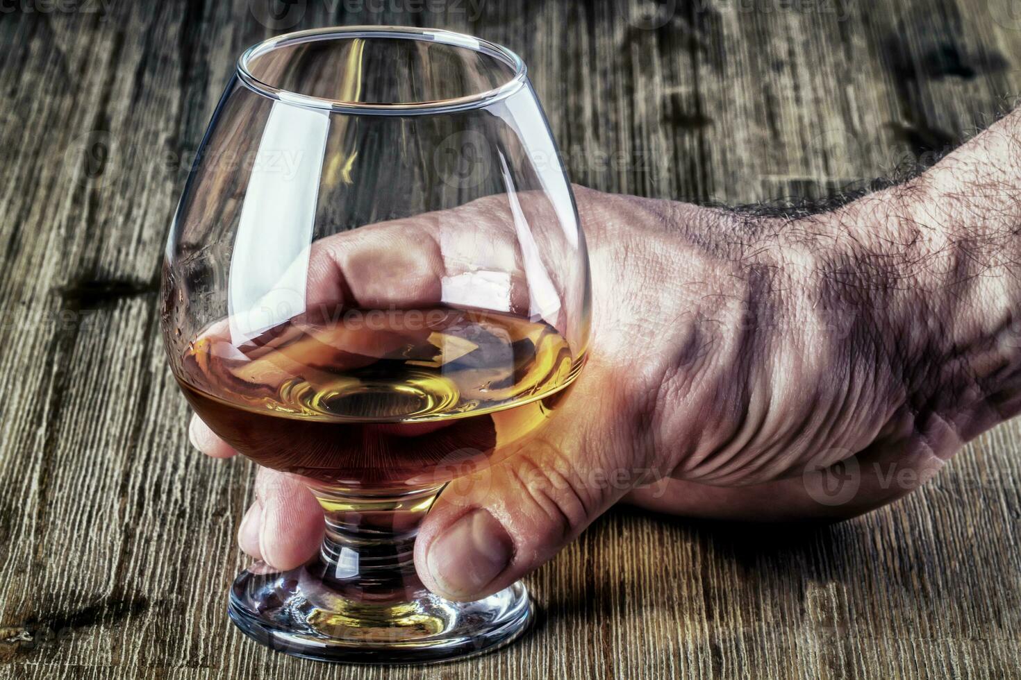 fuerte mans mano participación un elegante vaso de Ron o brandy en rústico antiguo de madera escritorio. foto