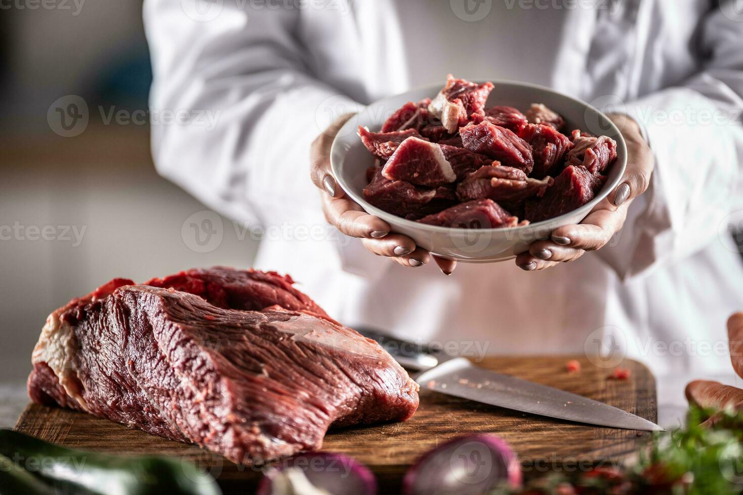 Small chunks of beef or pork for stew in a bowl next to a large piece of red meat on a cutting board photo
