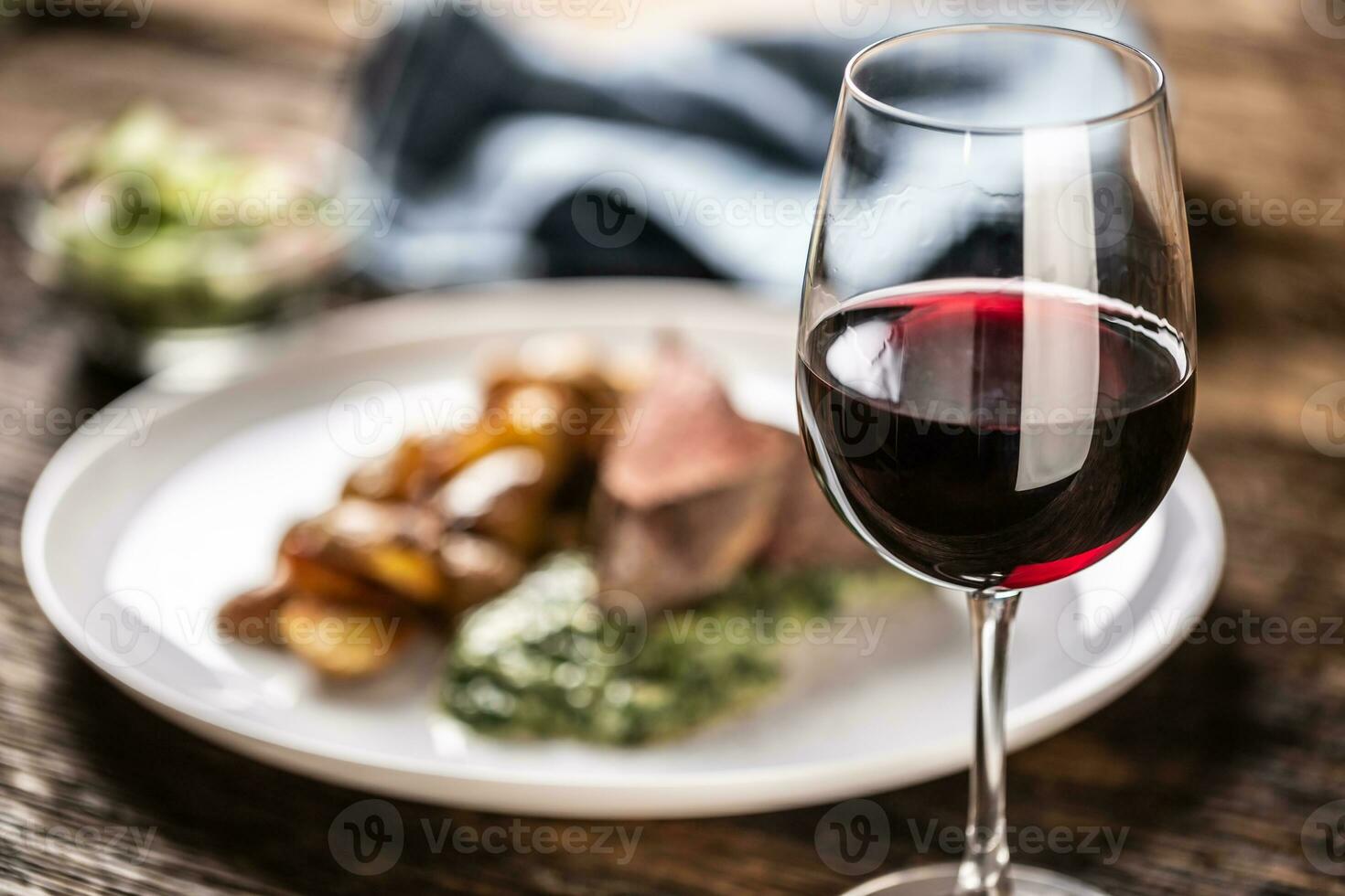 rojo vino como un típico baverage a un rojo carne filete con asado papas, Espinacas inmersión y Fresco ensalada servido en un blanco porcelana plato en el de madera escritorio. foto