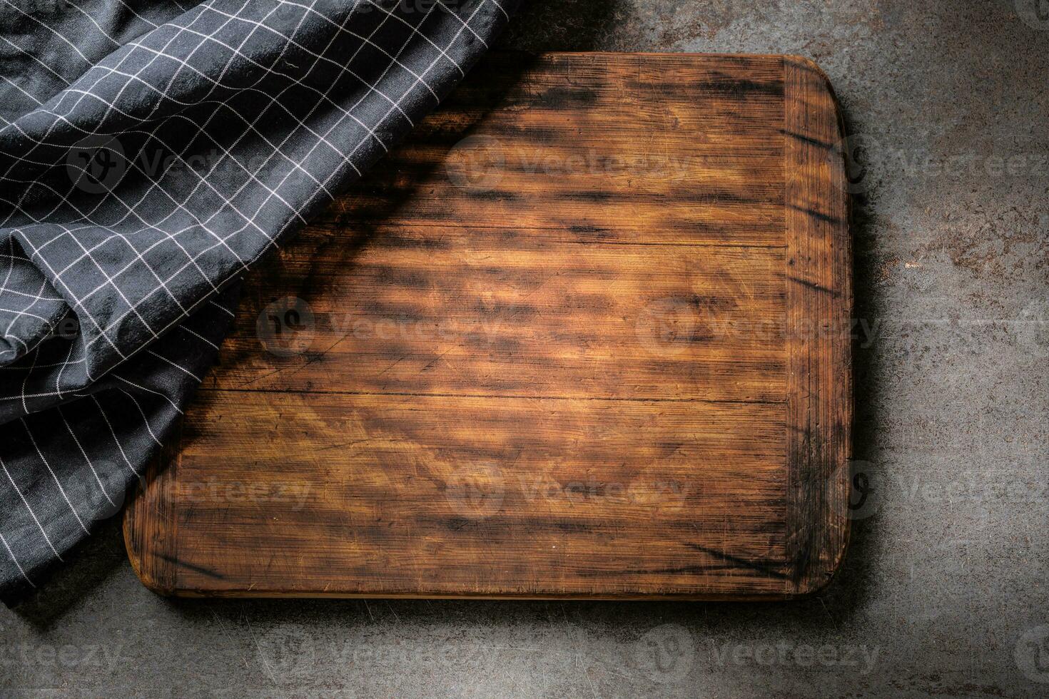 Top view of wooden dark brown vintage chopping board on dark metallic background with black checked cloth partial covering photo