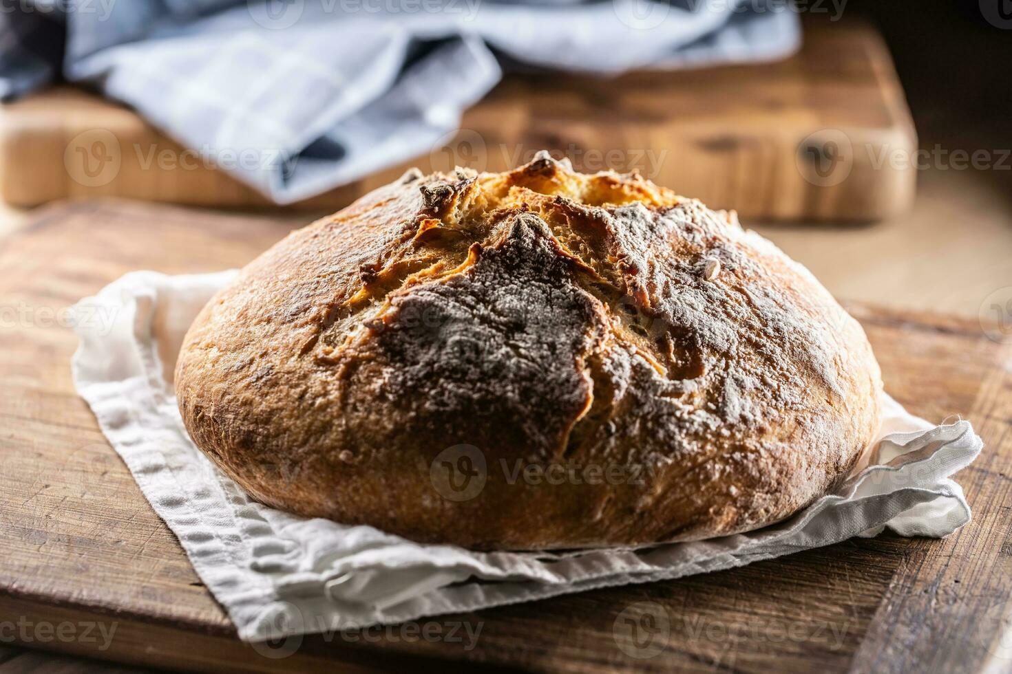 Homemade baked crusty bread places on a linen towel and wooden cutting board photo