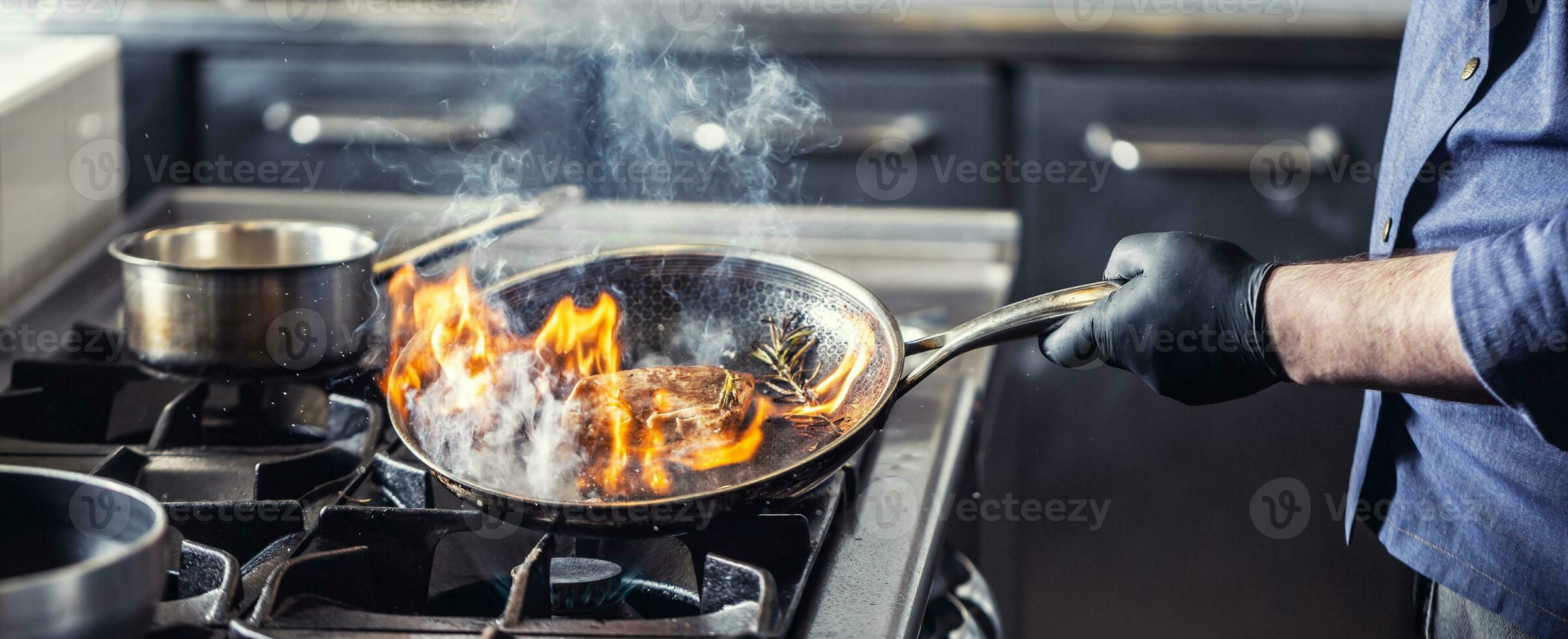 Chef in the kitchen leans pan to the side for alcohol in it to catch fire for gas stove, starting to flambe the food photo