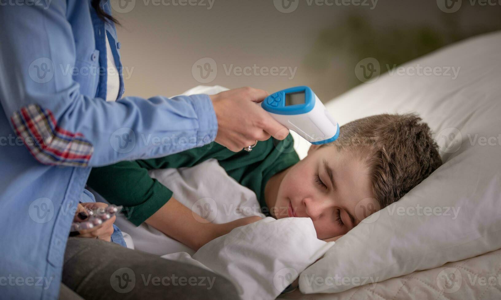 Mother uses thermometer to measure temperature of her sleeping boy in bed photo