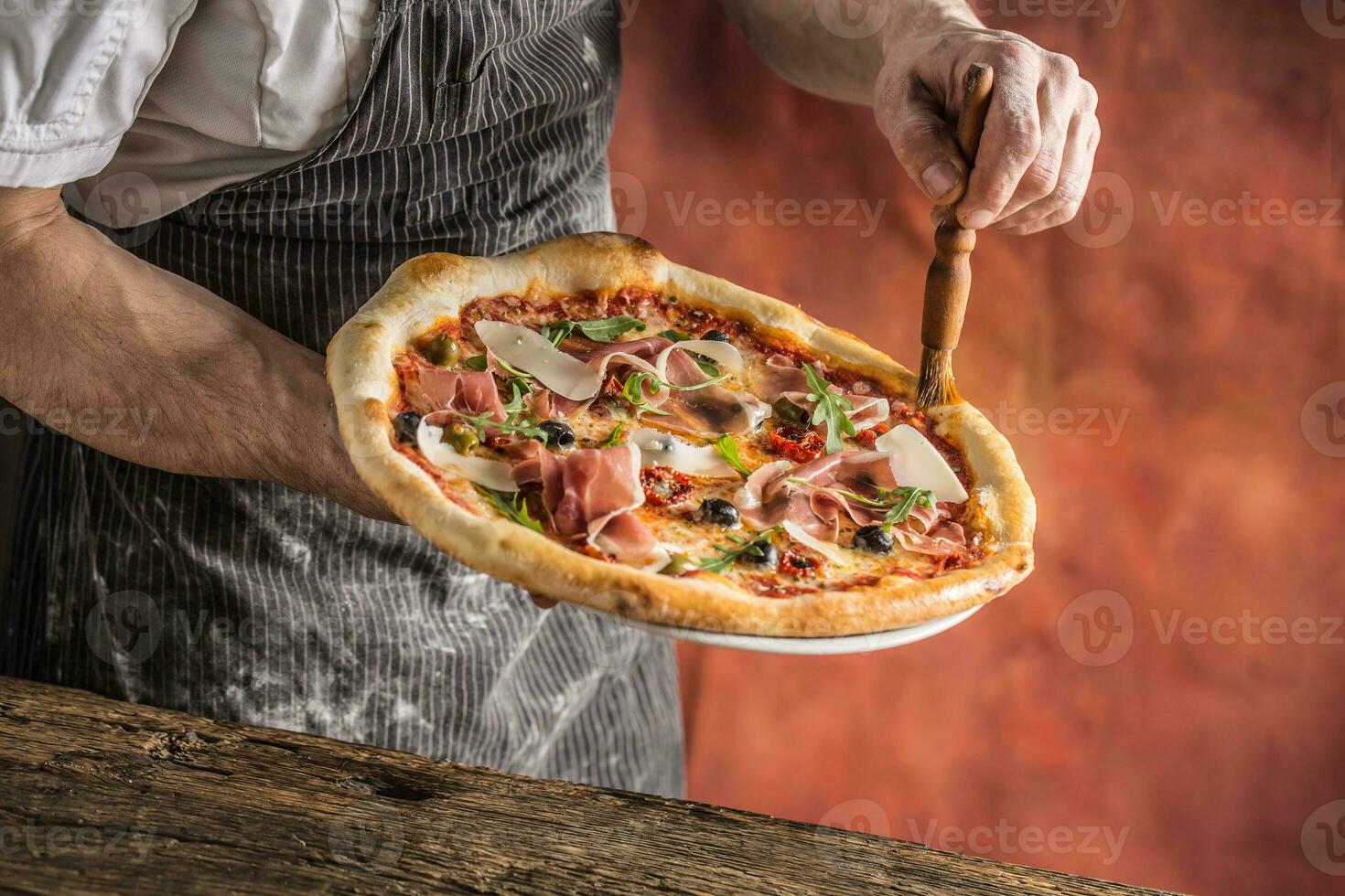 Pizza y cocinero. cocinero en el restaurante prepara un Pizza y decora eso con aceituna petróleo foto