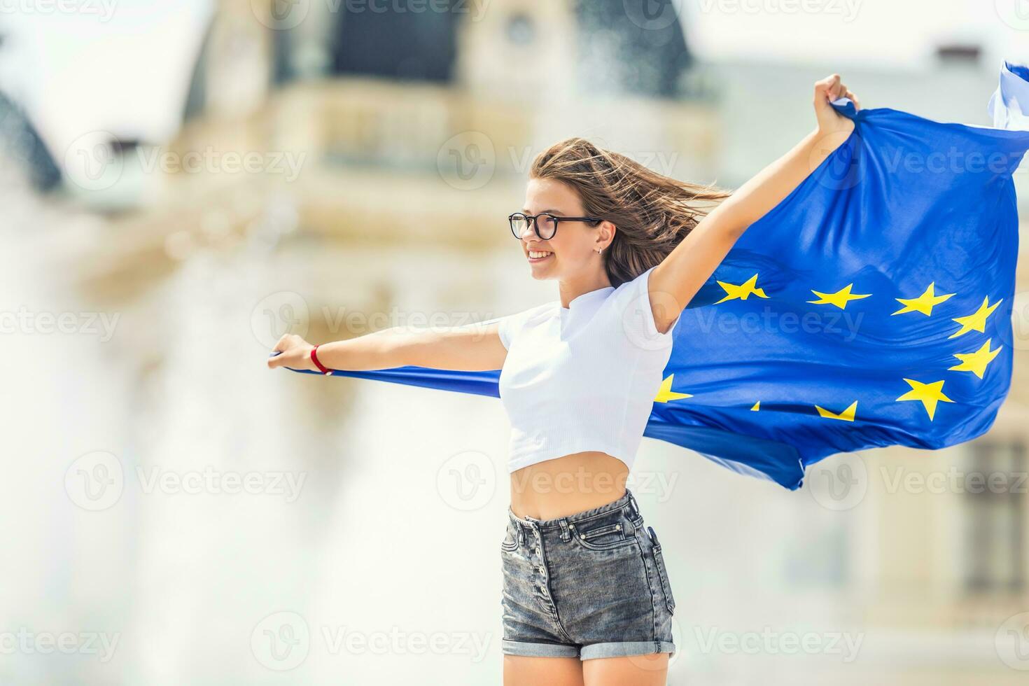 linda contento joven niña con el bandera de el europeo Unión en frente de un histórico edificio algun lado en Europa. foto