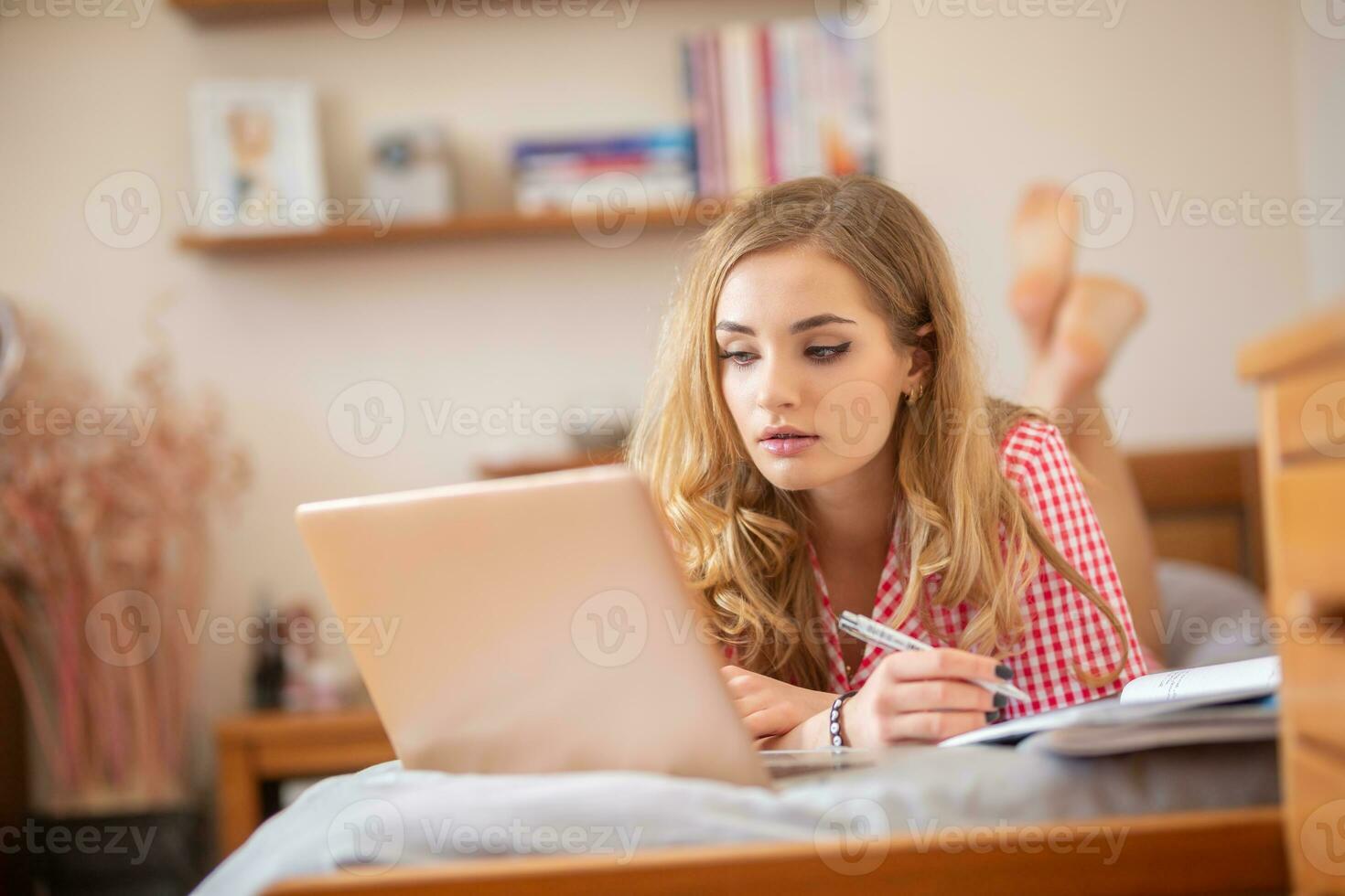 Motivated teen student lying on a bed solving assignements and having an online class from home due to global coronavirus pandemic photo