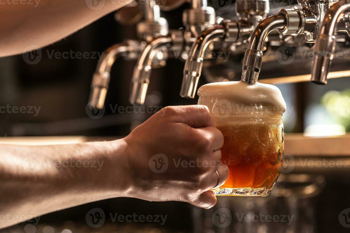 Hand holding mug of beer filled from the tap with foam floating out of the glass photo