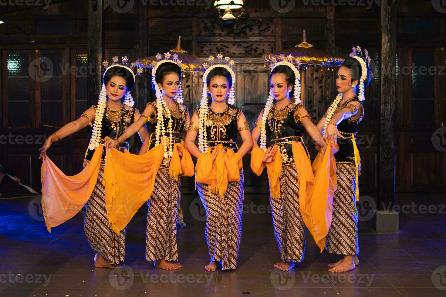 a group of Javanese dancers holding yellow shawls while dancing on stage photo