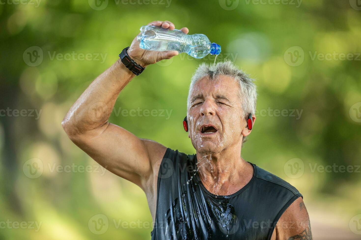 Pensioner male runner cools down by pouring fresh water from a bottle over his head photo