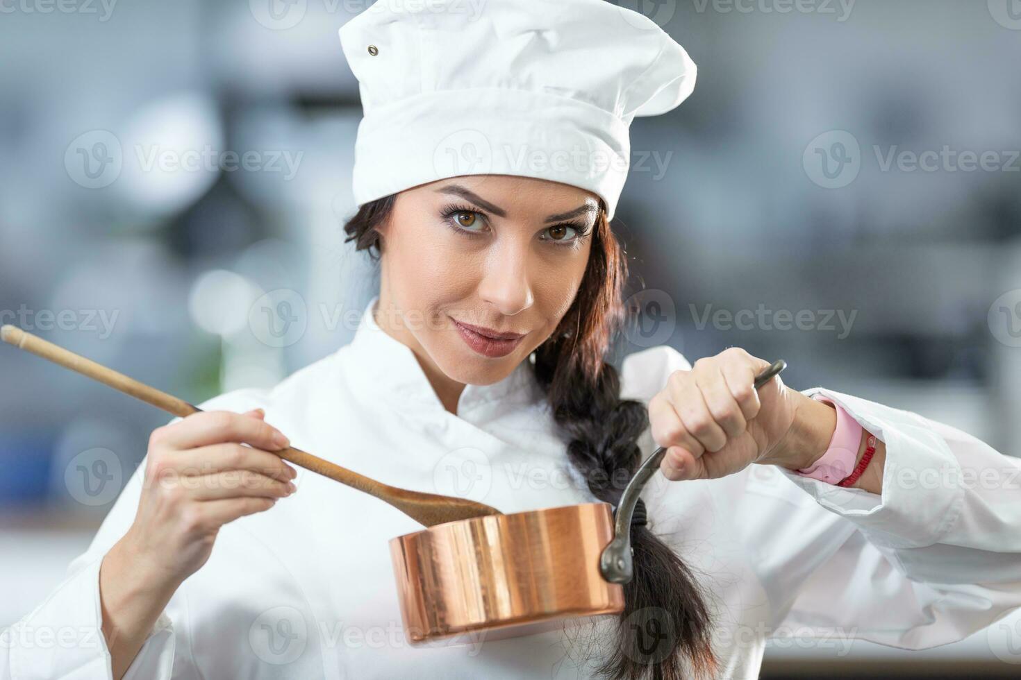 Beautiful female chef holds a copper pan and wooden spoon, earing a profesional overall photo