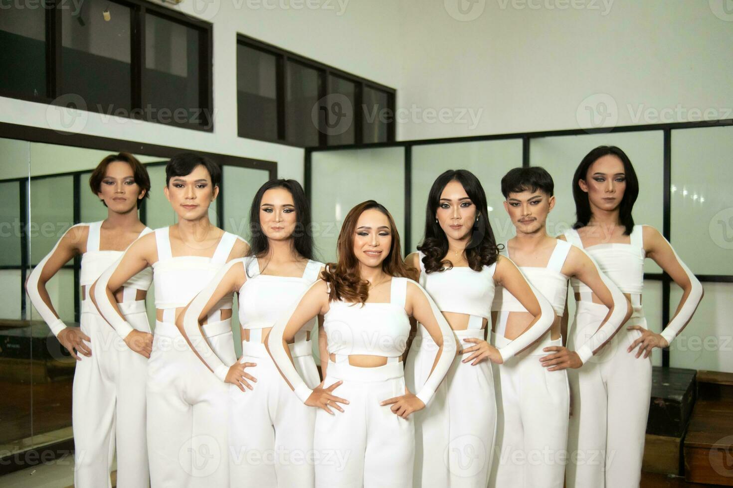 a group of Asian dancers stand side by side in white costumes in a room with a dance floor photo