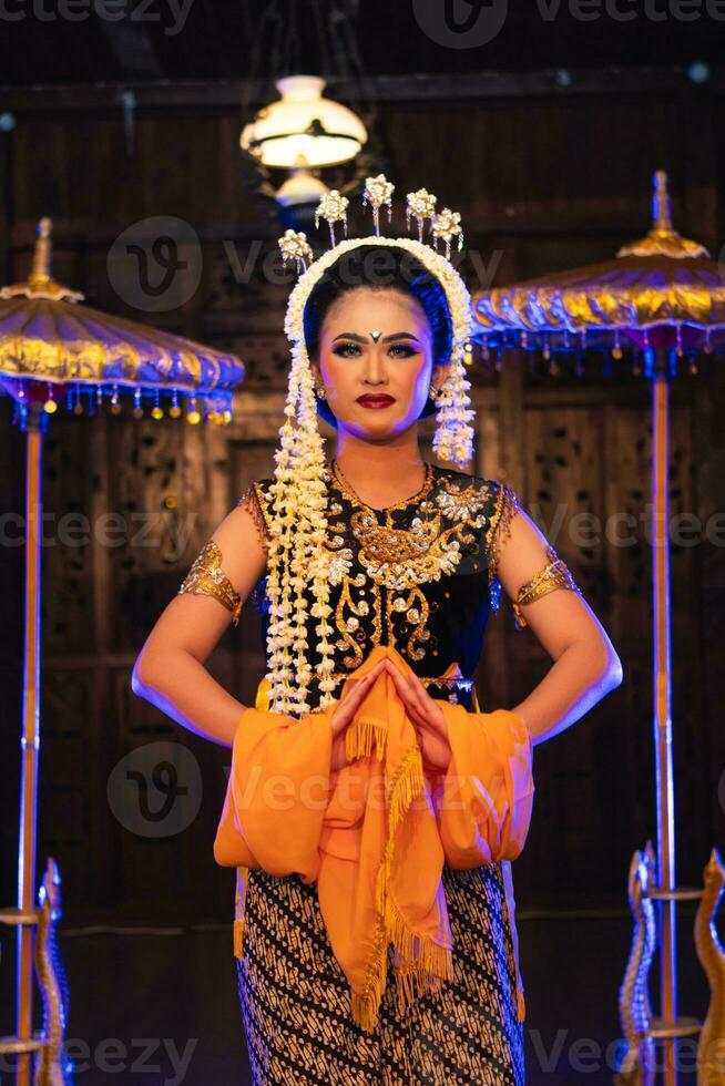 a Javanese dancer dances in a golden costume and a yellow shawl on stage photo