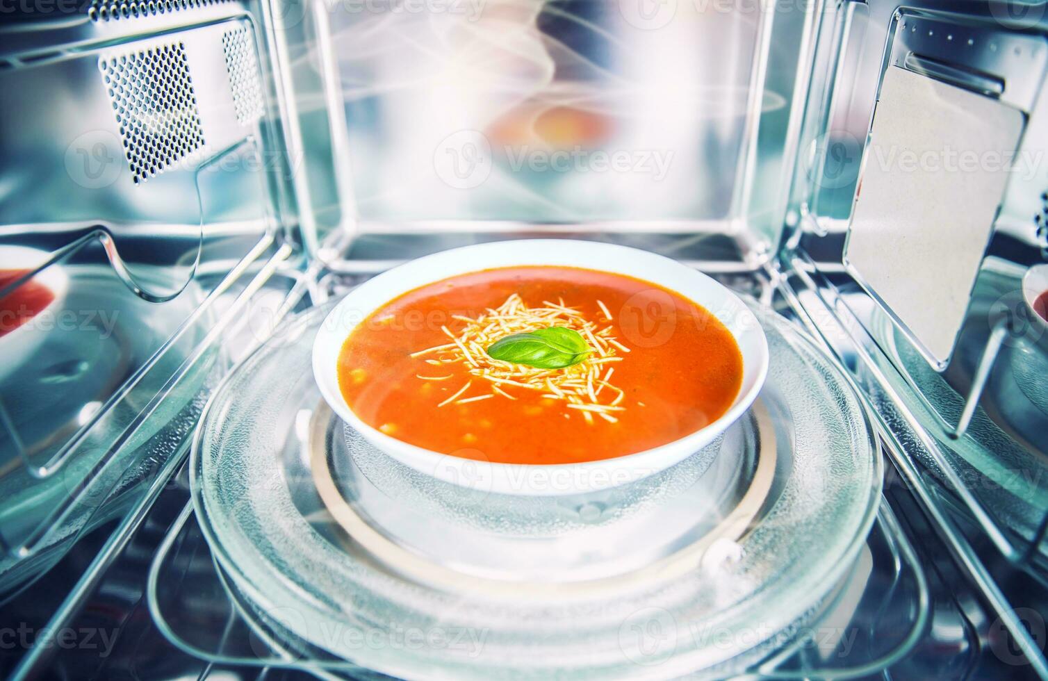 Inside view of new clean staniless microwave oven with a tomato soup in white plate photo