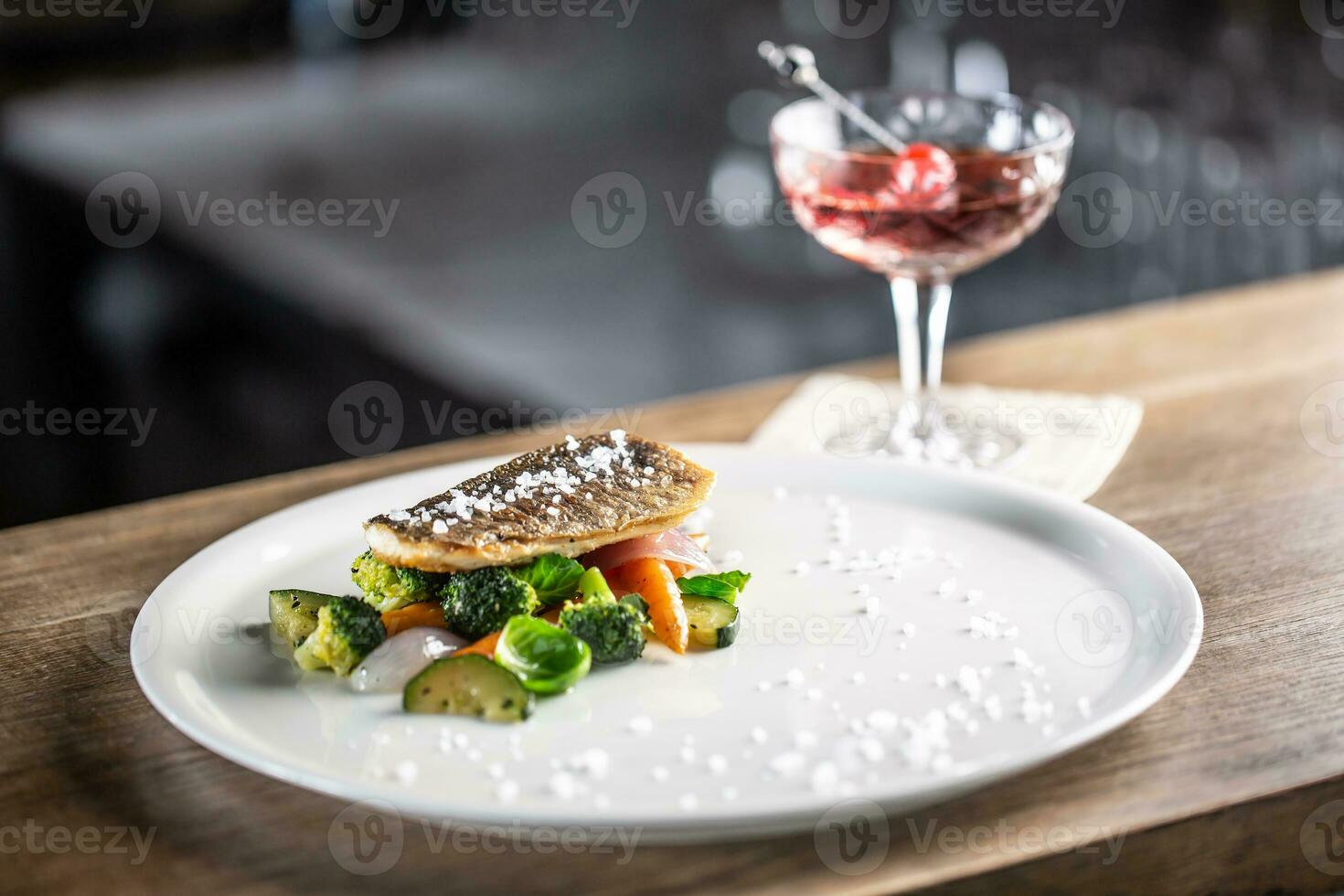 Healthy fish cooked with steamed vegetables served on a plate next to a negroni cocktail photo