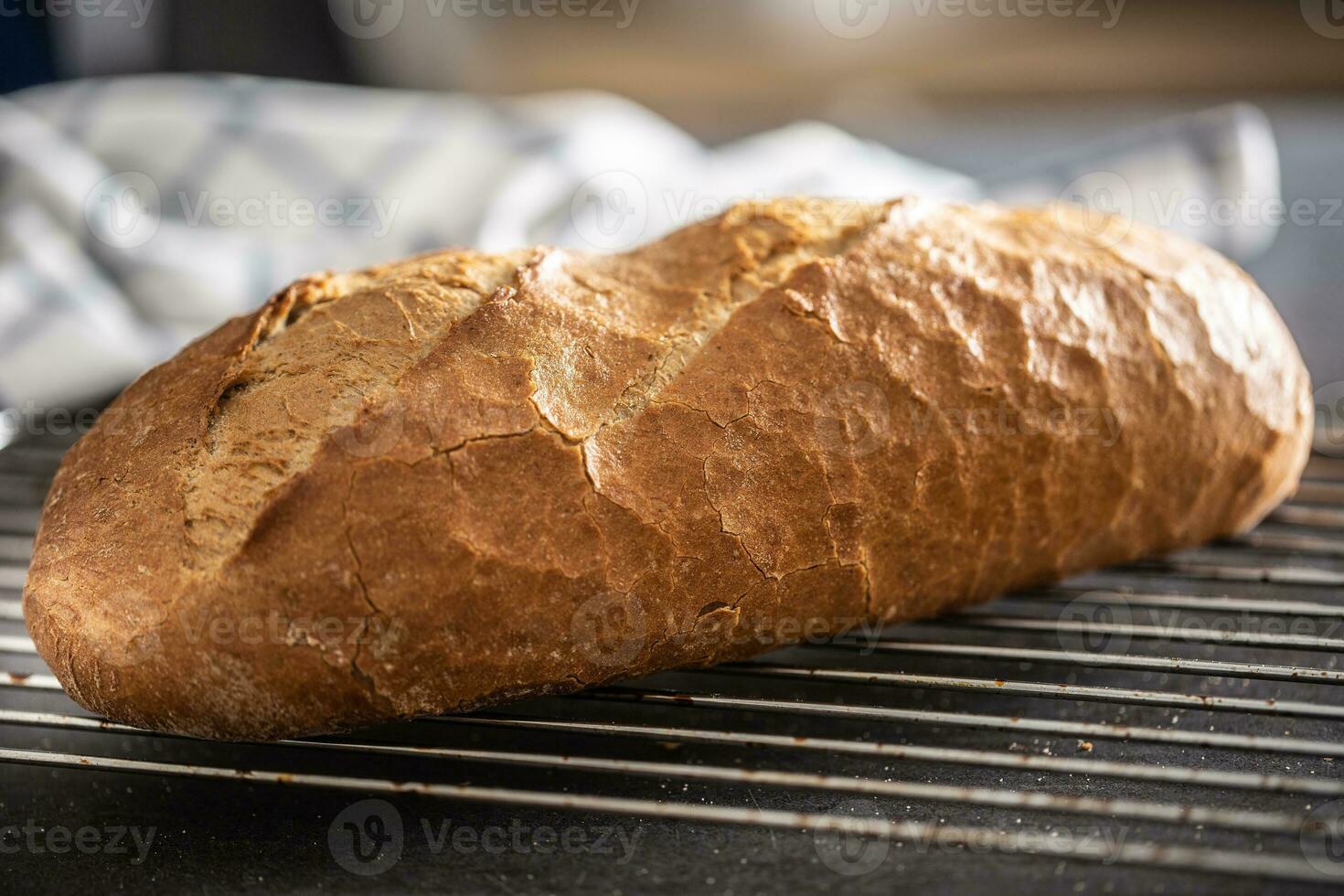 Fresh crusty bread loaf placed on a metal grid in the kitchen photo