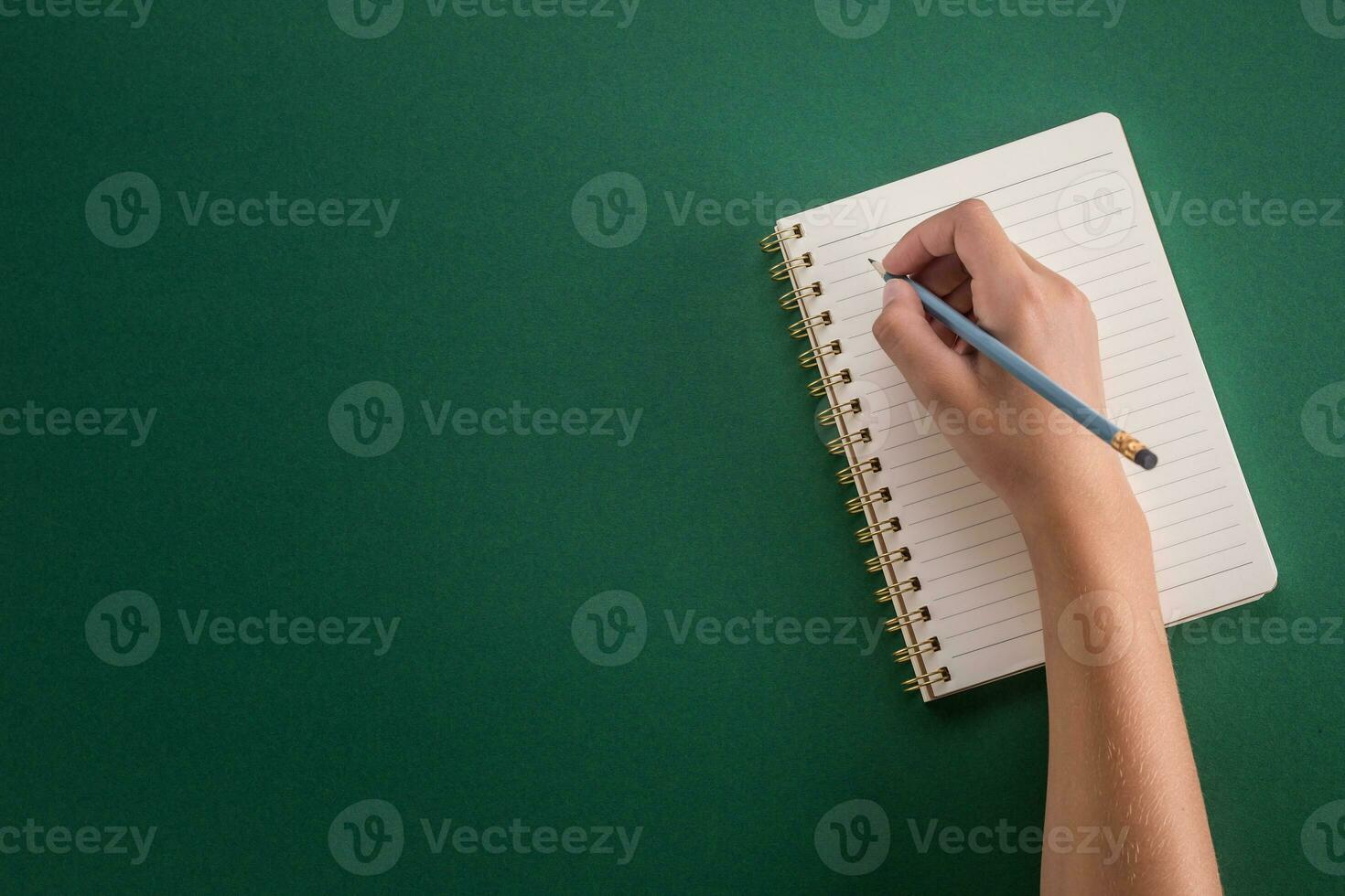 Student of the girl hand from a pencil with notebook on a green background photo