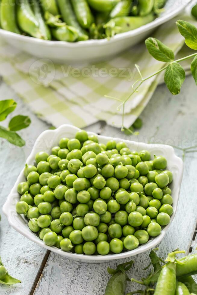 Green raw peas and pods in pocelain bow isolated on wooden table photo