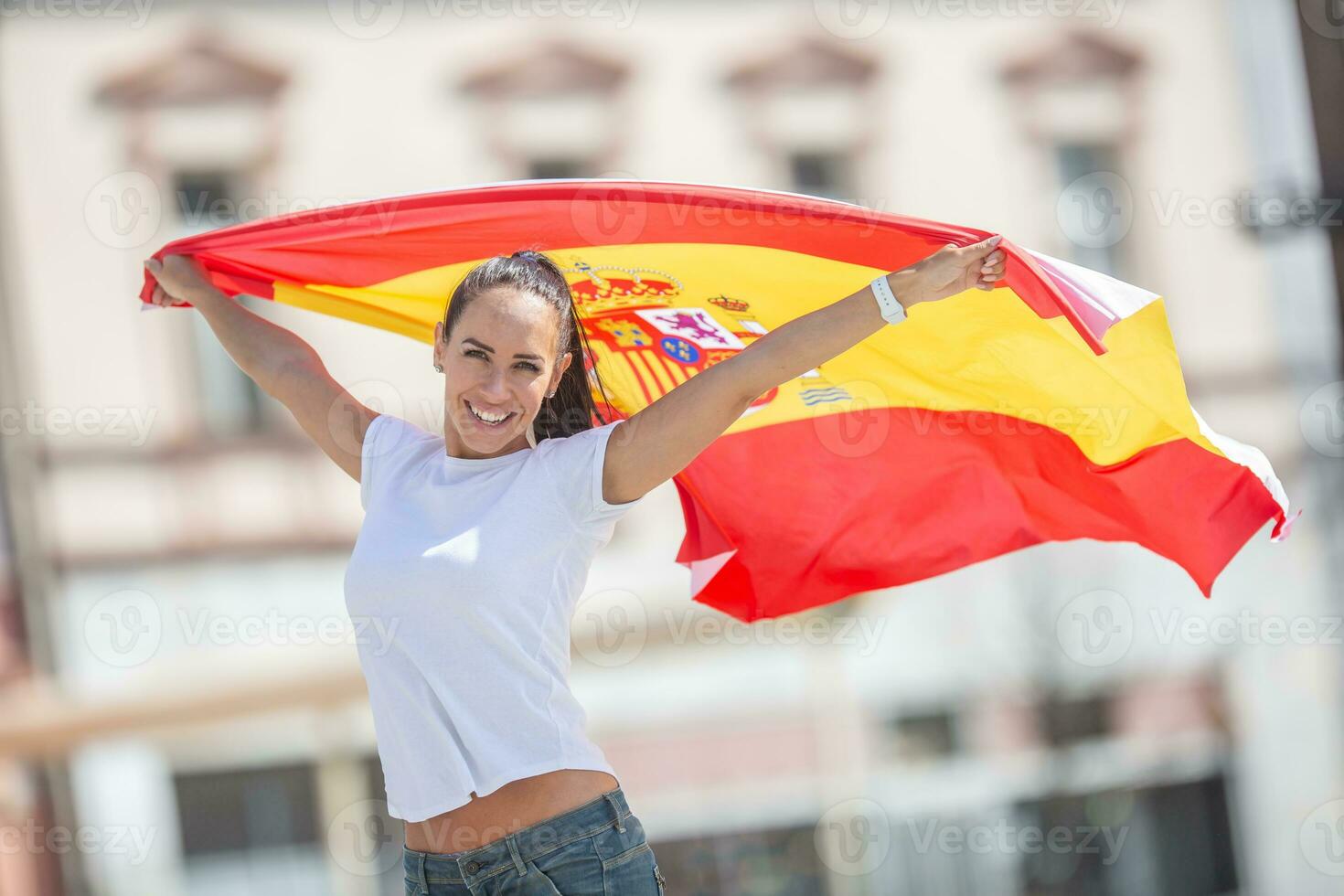 Beautiful girl holds a Spanish flag in her hands behind her, cheering on a street photo