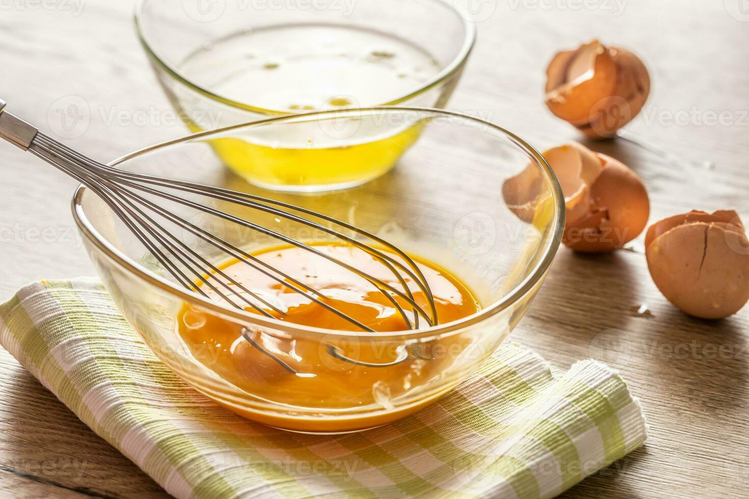 Whisked egg yolks in a glass bowl with egg whites in a second bowl and crackjed egg shells on the side photo