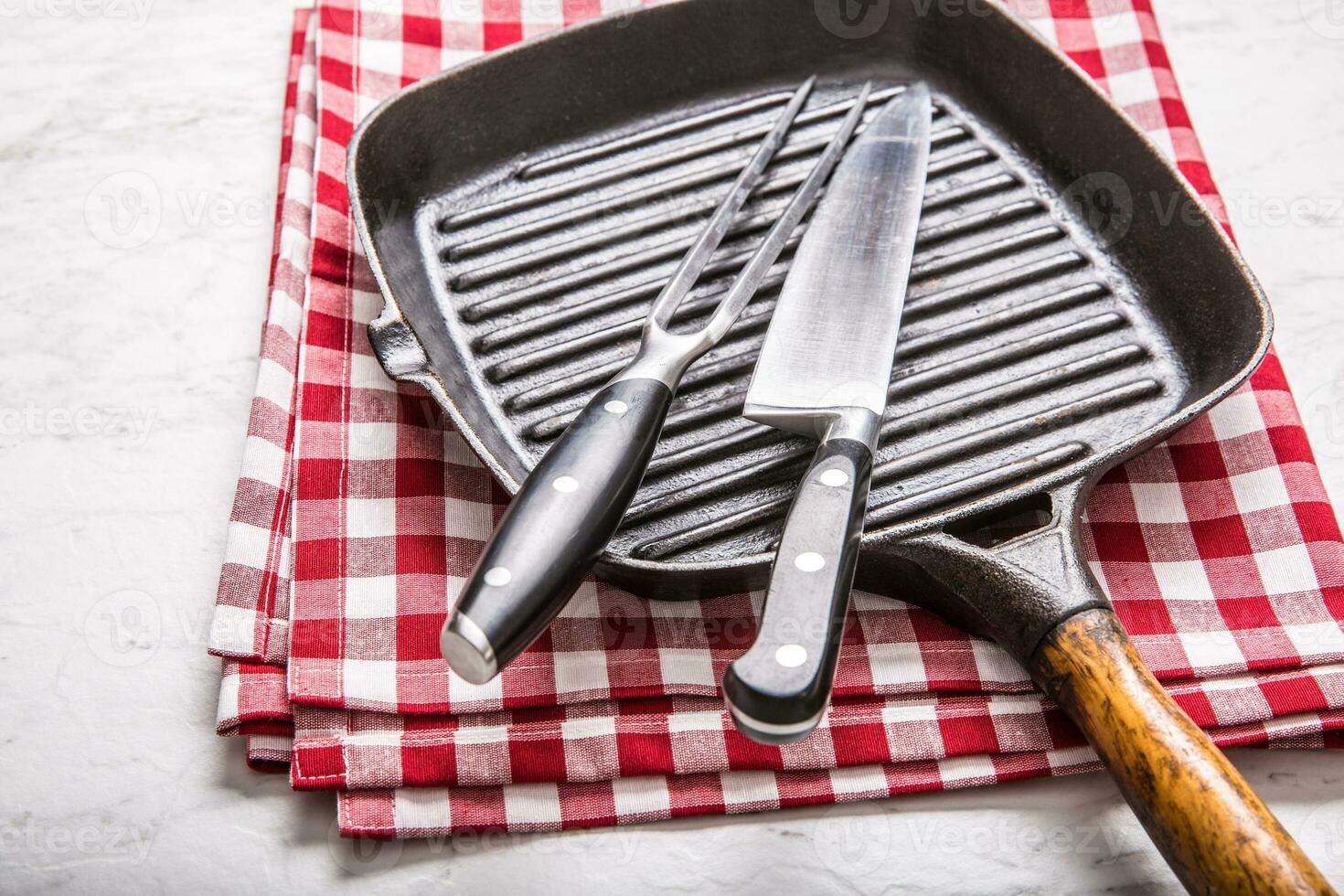 Empty grill pan on marble table with red tablecloth knife and fork photo
