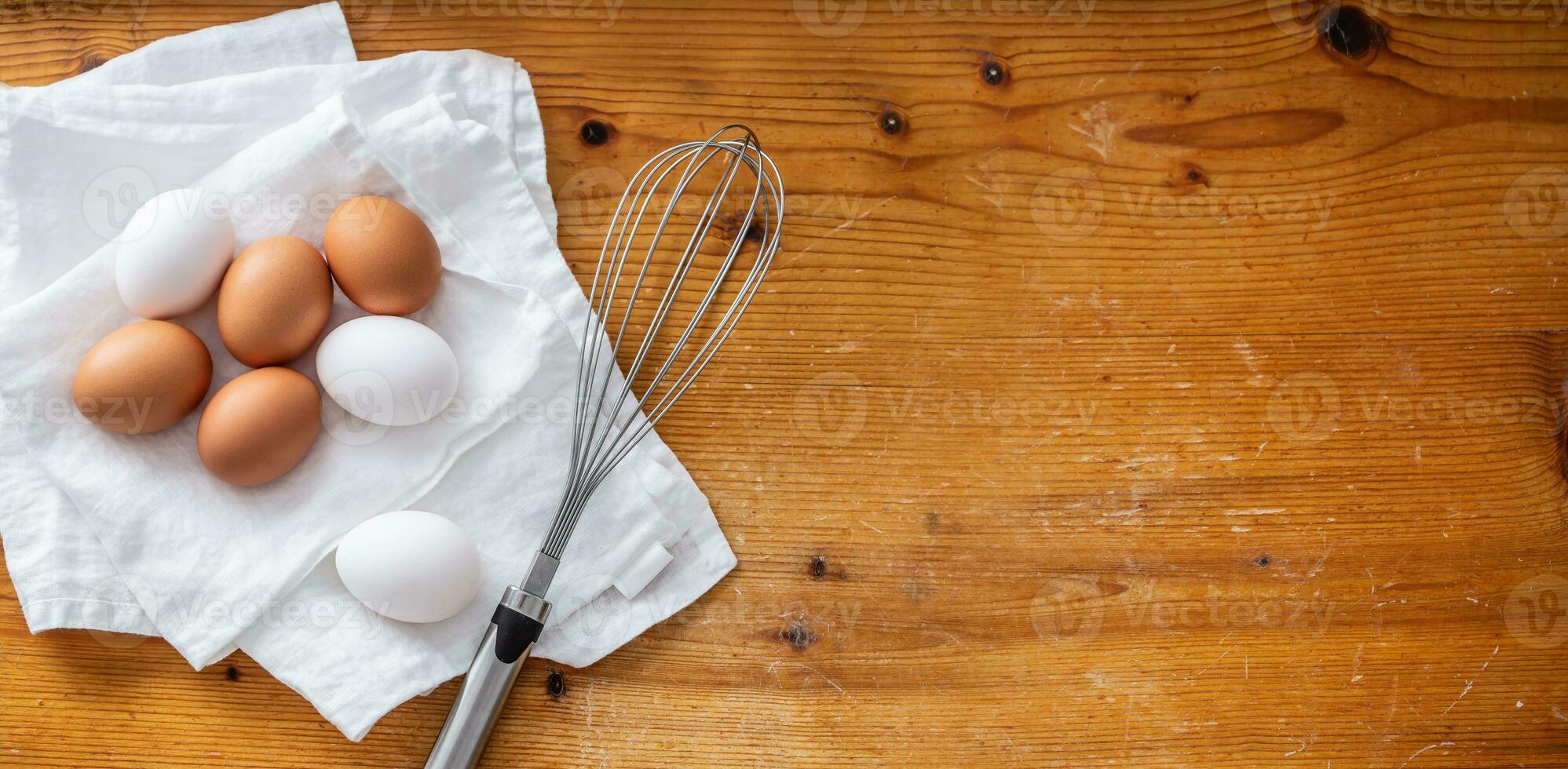 Top view of three white and four brown eggs on a clean white cloth next to a whisker. photo