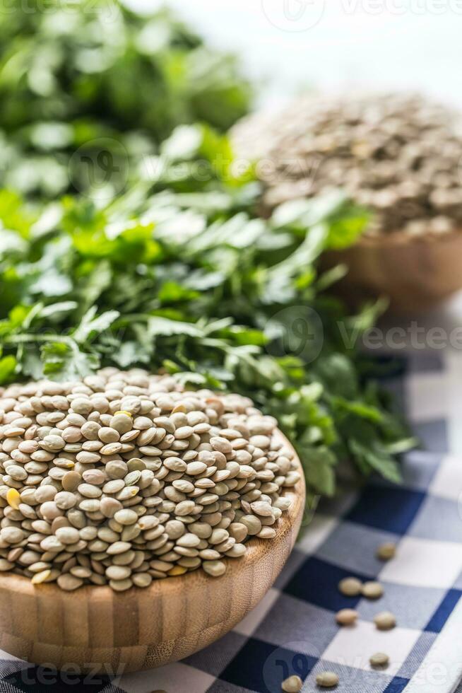 Uncooked lentils in wooden bowles  with parsley herbs on kitchen photo