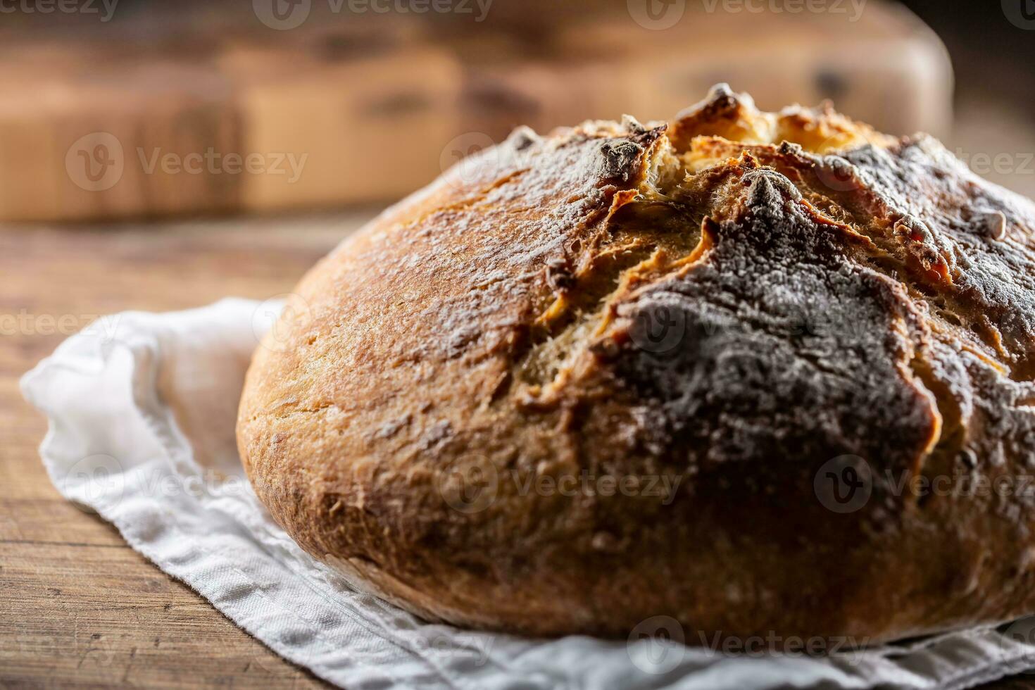 Homemade baked crusty bread places on a linen towel and wooden cutting board photo