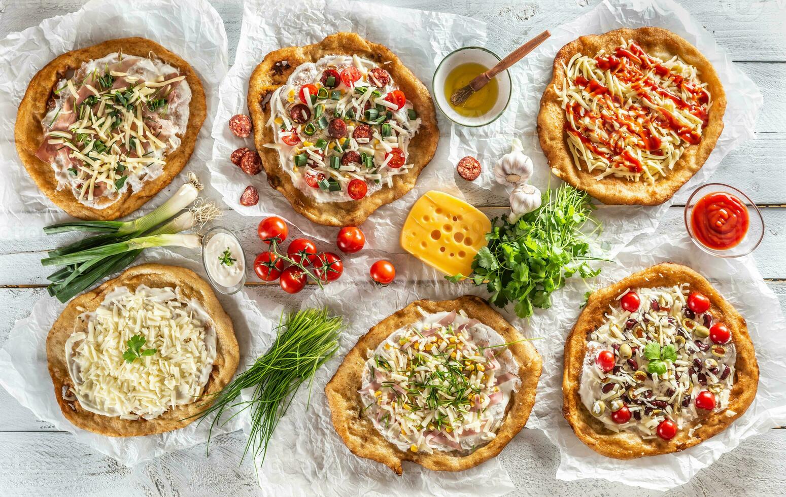 A close up a set of hungarian traditional langos with crusty garlic edges served with vegetables, cream sausages, herbs, grated, cheese, ketchup and dips and oil photo