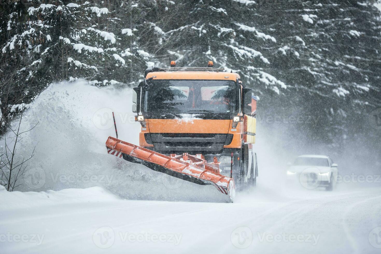 Snowplow clearing road from snow in the forest with traffic lining up behind the truck photo