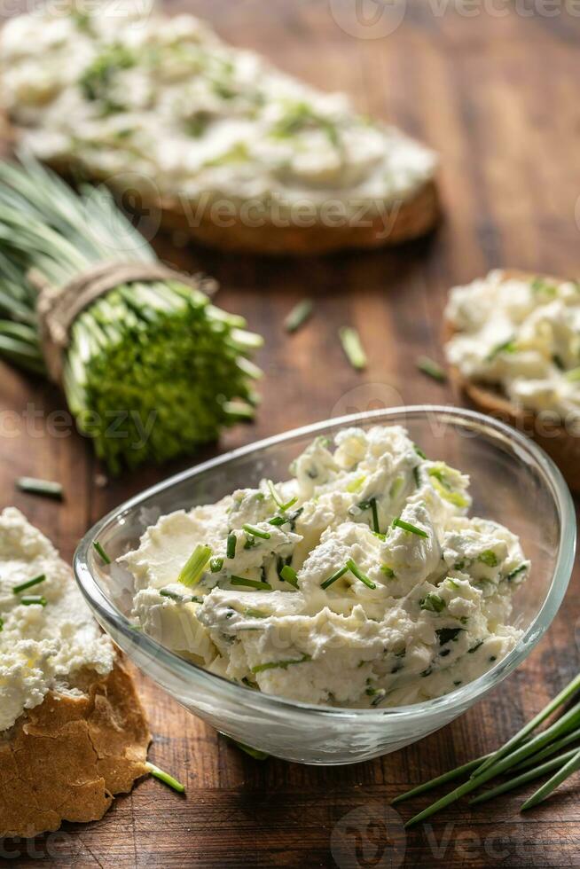 Portrait of a bowl of homemade cream cheese spread with chopped chives surrounded by bread slices with spread and a bunch of freshly cut chives photo