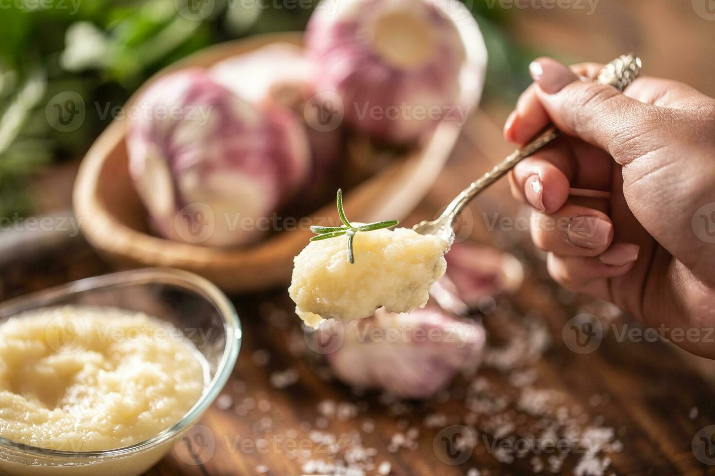 Detail of a teaspoon of garlic paste with fresh garlic in the background photo