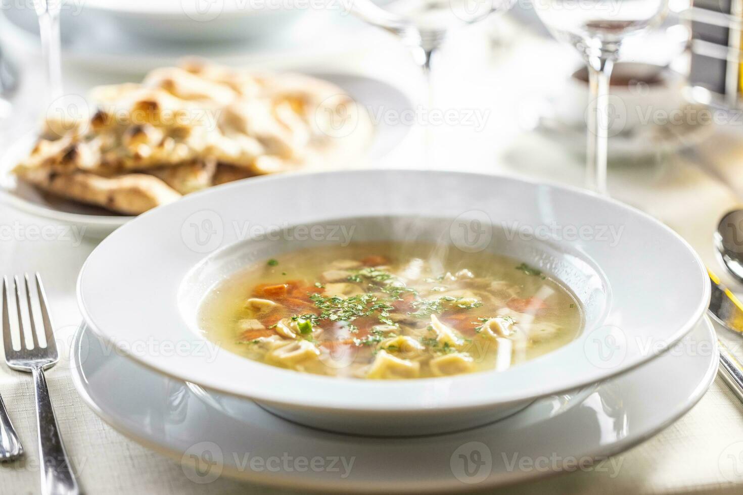 Hot chicken soup with small tortellini, carrot and greens on top photo