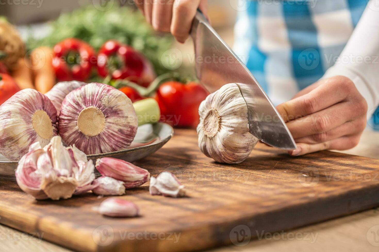 Detail of garlic head being cut to half with more fresh unpeeled garlic on the side and various veg in the background photo