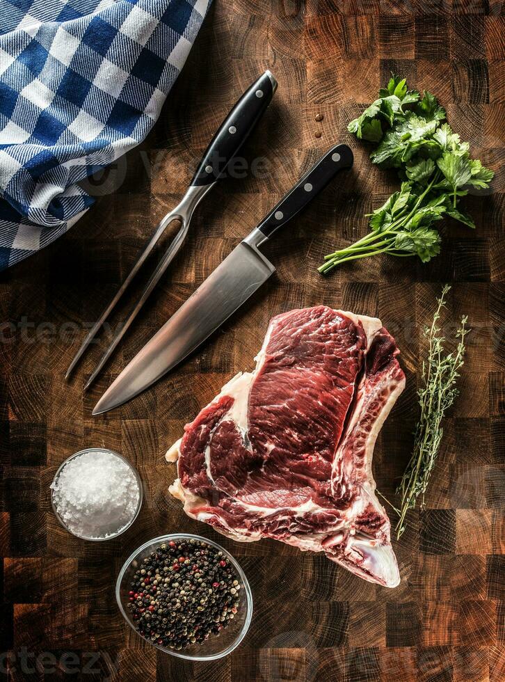 costilla ojo filete con hueso en Carnicero tablero con hierbas sal pimienta tenedor y cuchillo foto