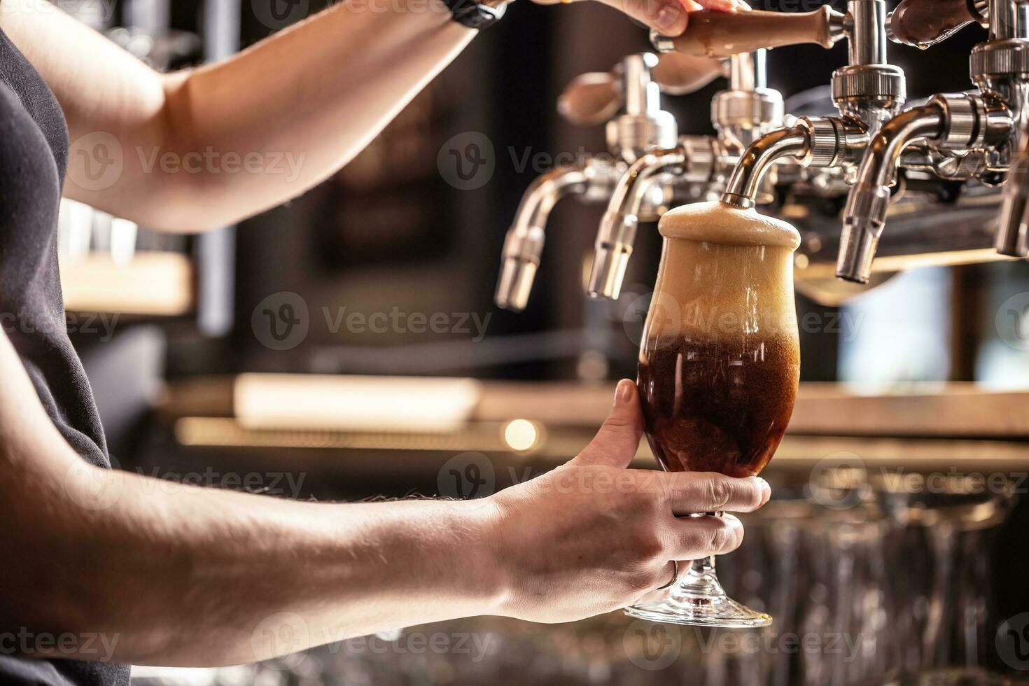 Foam on dark beer is about to pour out of the glass tapped with the alcoholic beverage photo