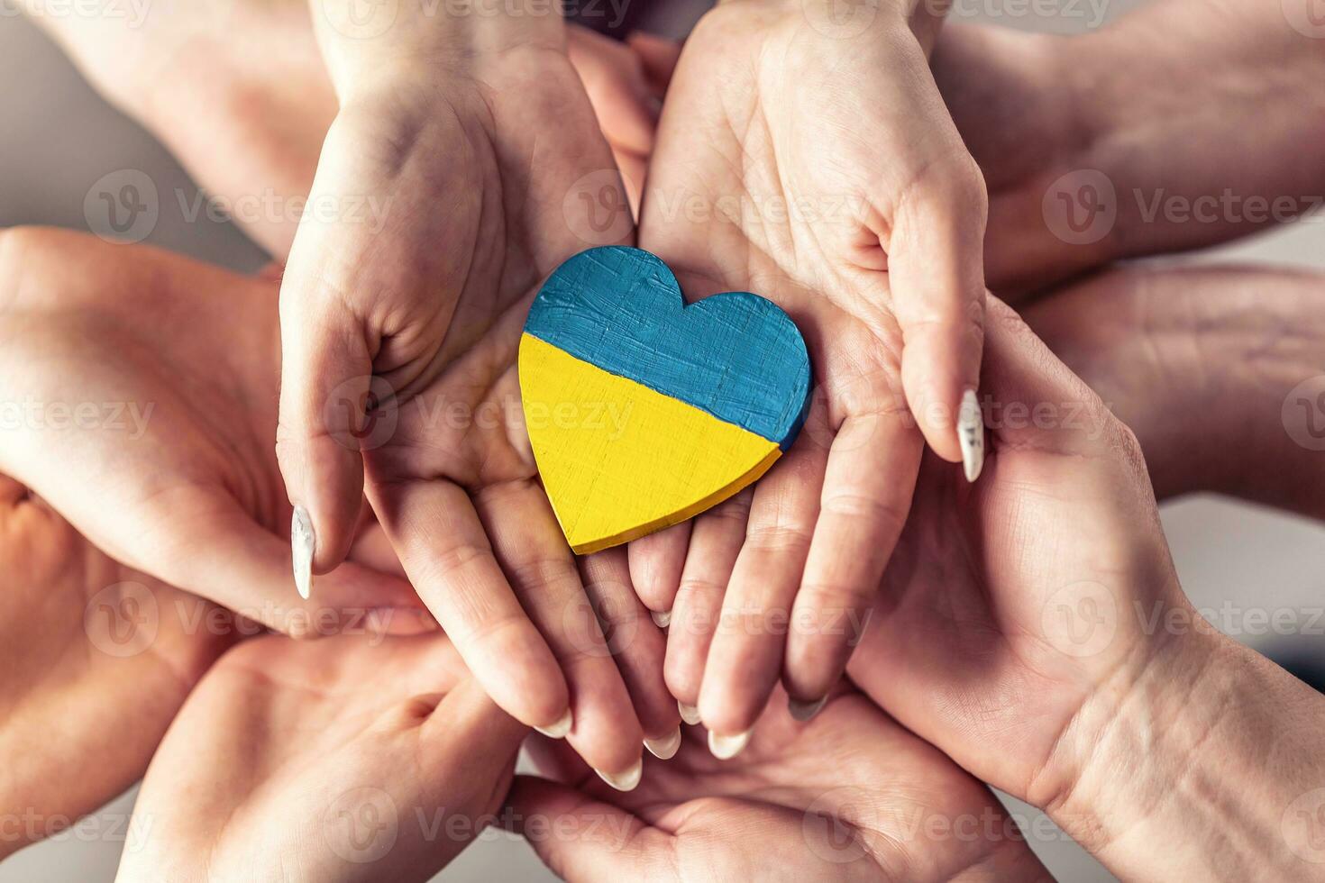 We stand with Ukraine symbol as numerous hands hold one another in unity with a wooden heart painted in Ukrainian flag colors on top photo