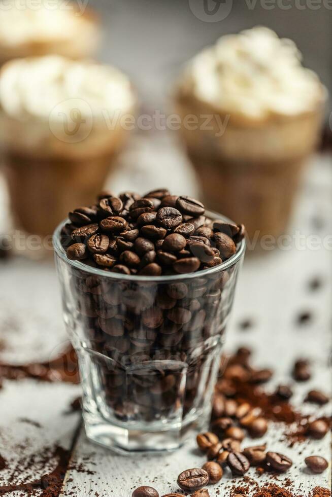 Coffee beans in a glass cup and in the background a cup with coffee and whipped cream photo